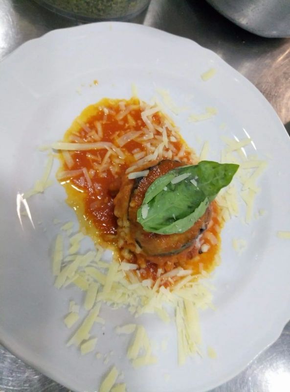 Melanzane impilate con salsa di pomodoro, formaggio e basilico su un piatto bianco.