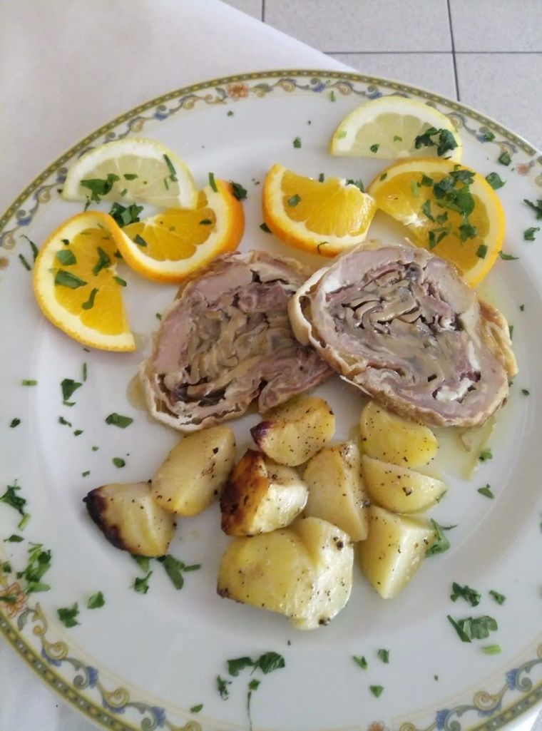 Piatto di carne ripiena affettata con patate arrosto e fette d'arancia, guarnito con prezzemolo.