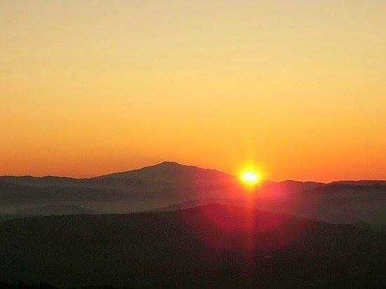 Tramonto sulle montagne, sole che emerge con brillanti tonalità arancioni e rosse.