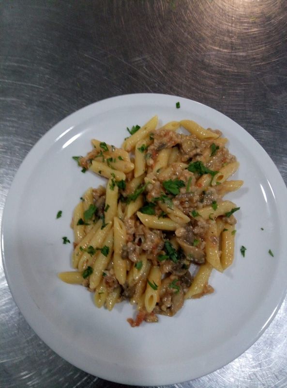 Penne al ragù, guarnite con prezzemolo, servite su un piatto bianco.