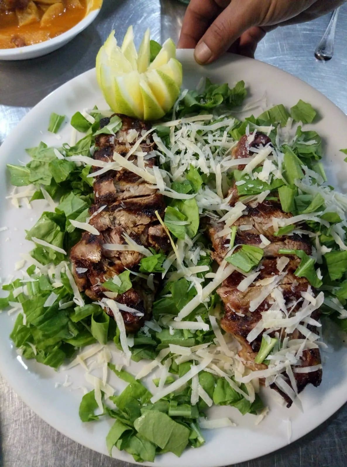 Fette di carne grigliate su rucola, guarnite con formaggio ed erbe verdi, presentate su un piatto bianco.