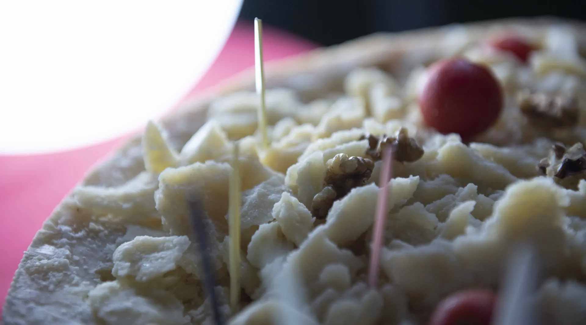 Primo piano di una torta ricoperta di glassa bianca, noci e frutti di bosco rossi, con stuzzicadenti.