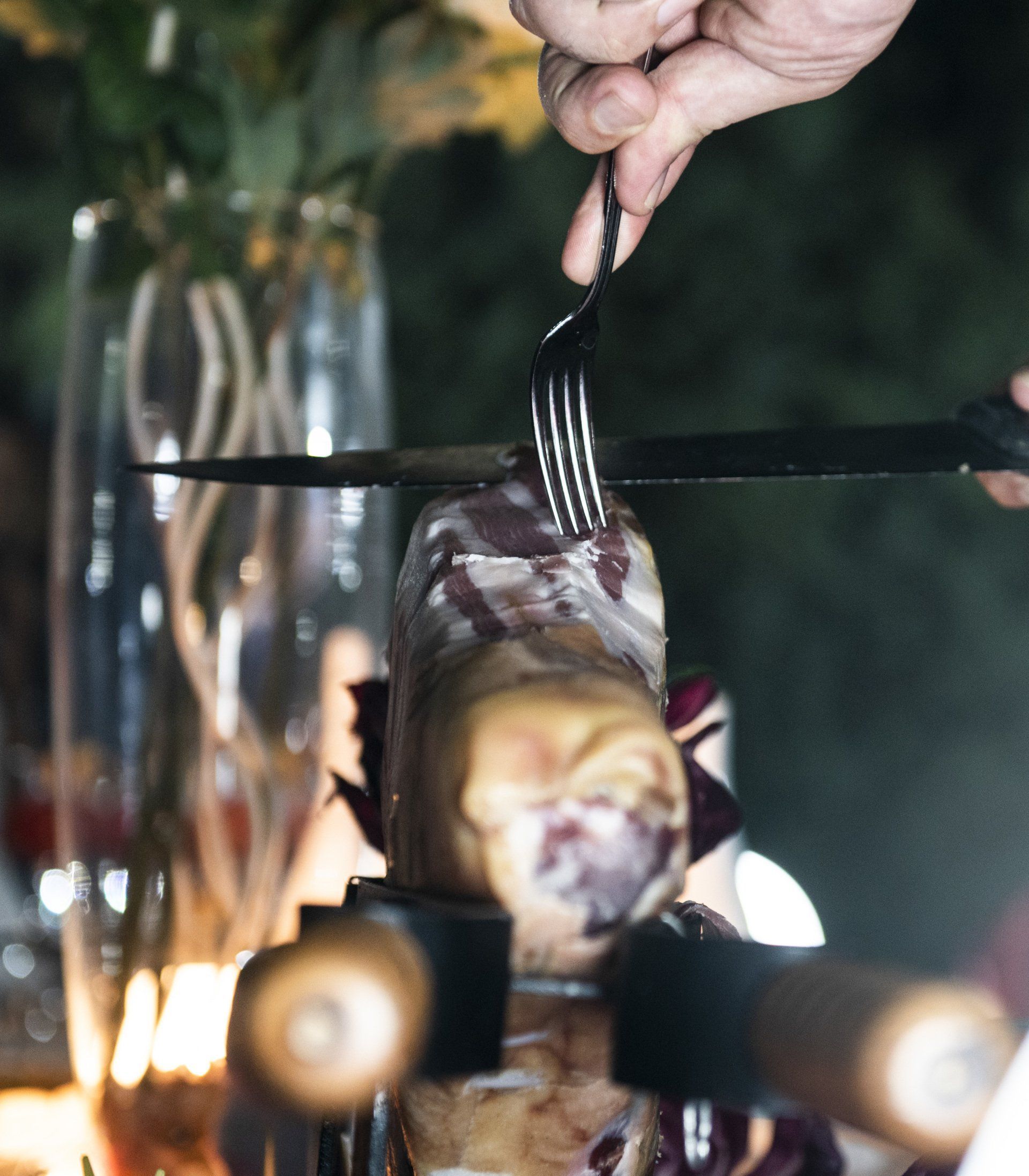 Persona che taglia carne arrostita con forchetta e coltello all'aperto.