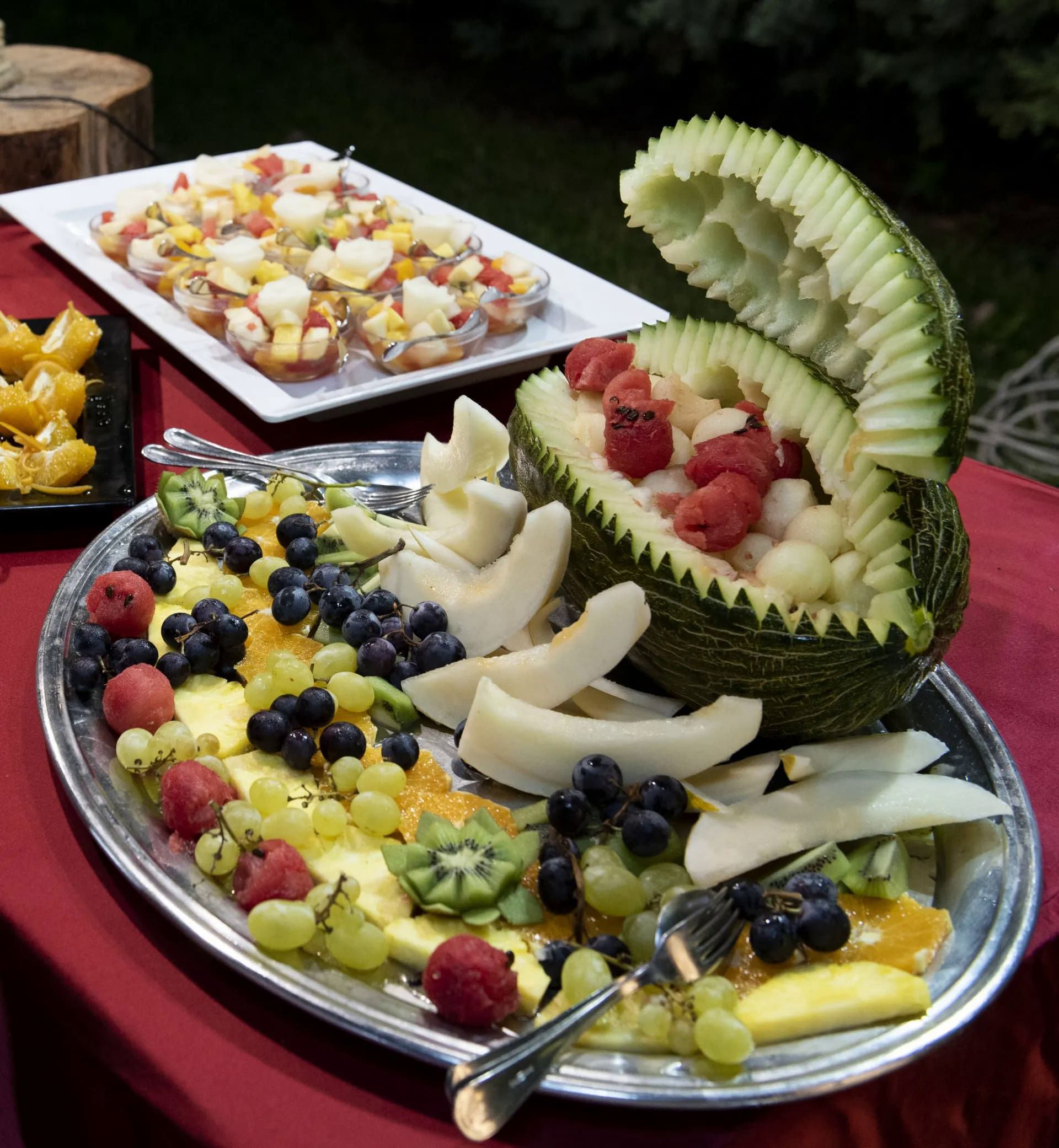 Piatto di frutta con intaglio di melone e frutta assortita: uva, lamponi, melone cantalupo, kiwi.