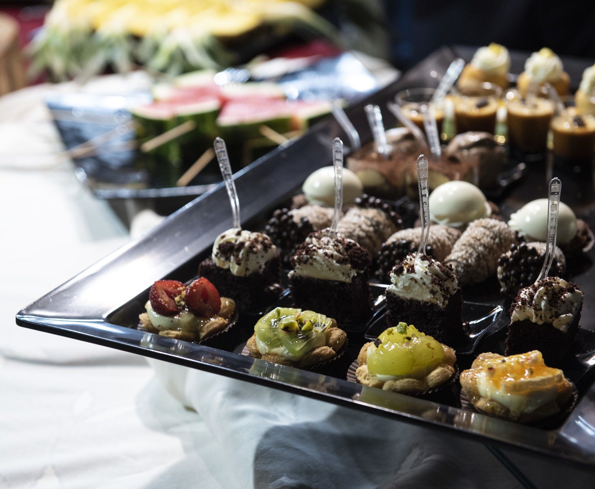 Vassoio di dessert assortiti: crostate, brownies e cannoli. Un altro vassoio con fette di anguria.