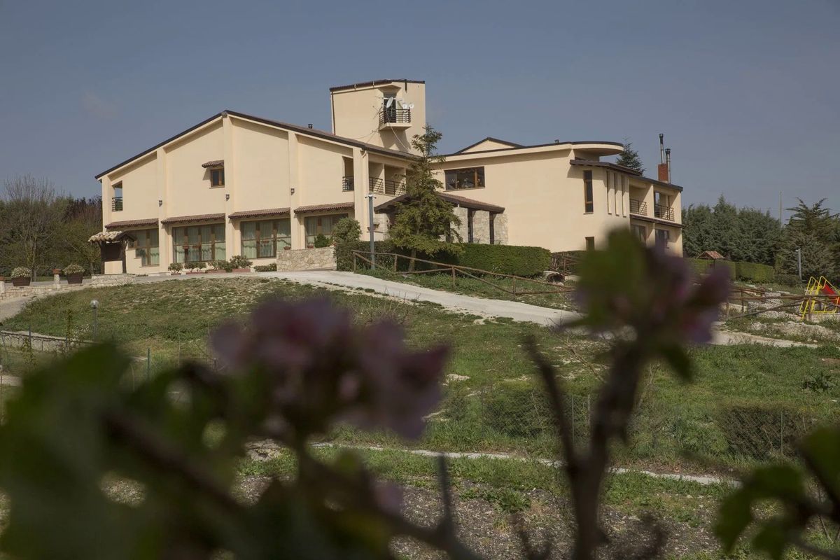 Edificio beige con una torre su una collina erbosa, visto da dietro fiori rosa sfocati in una giornata di sole.