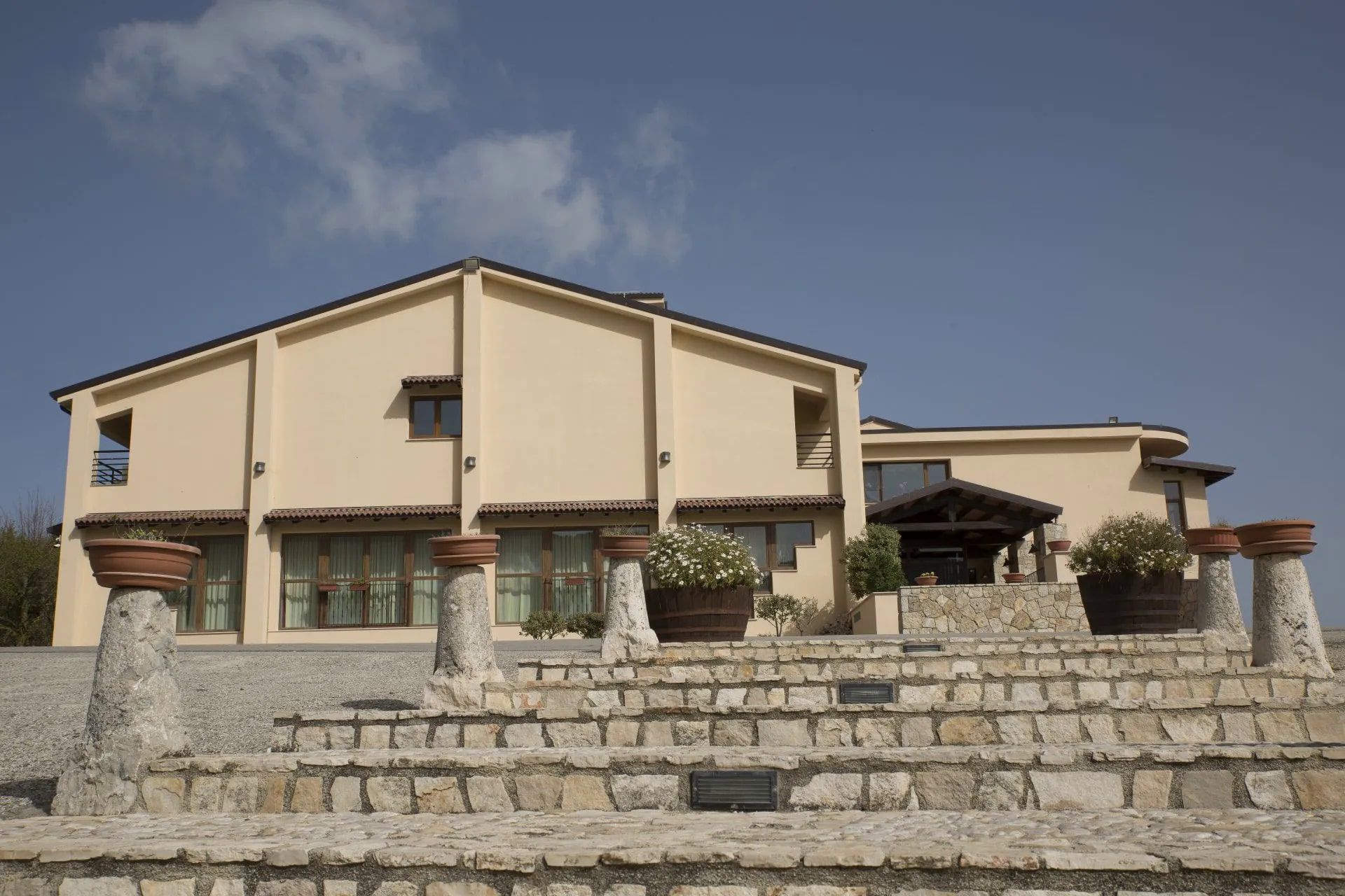 Edificio beige con gradini in pietra, fioriere e cielo azzurro.