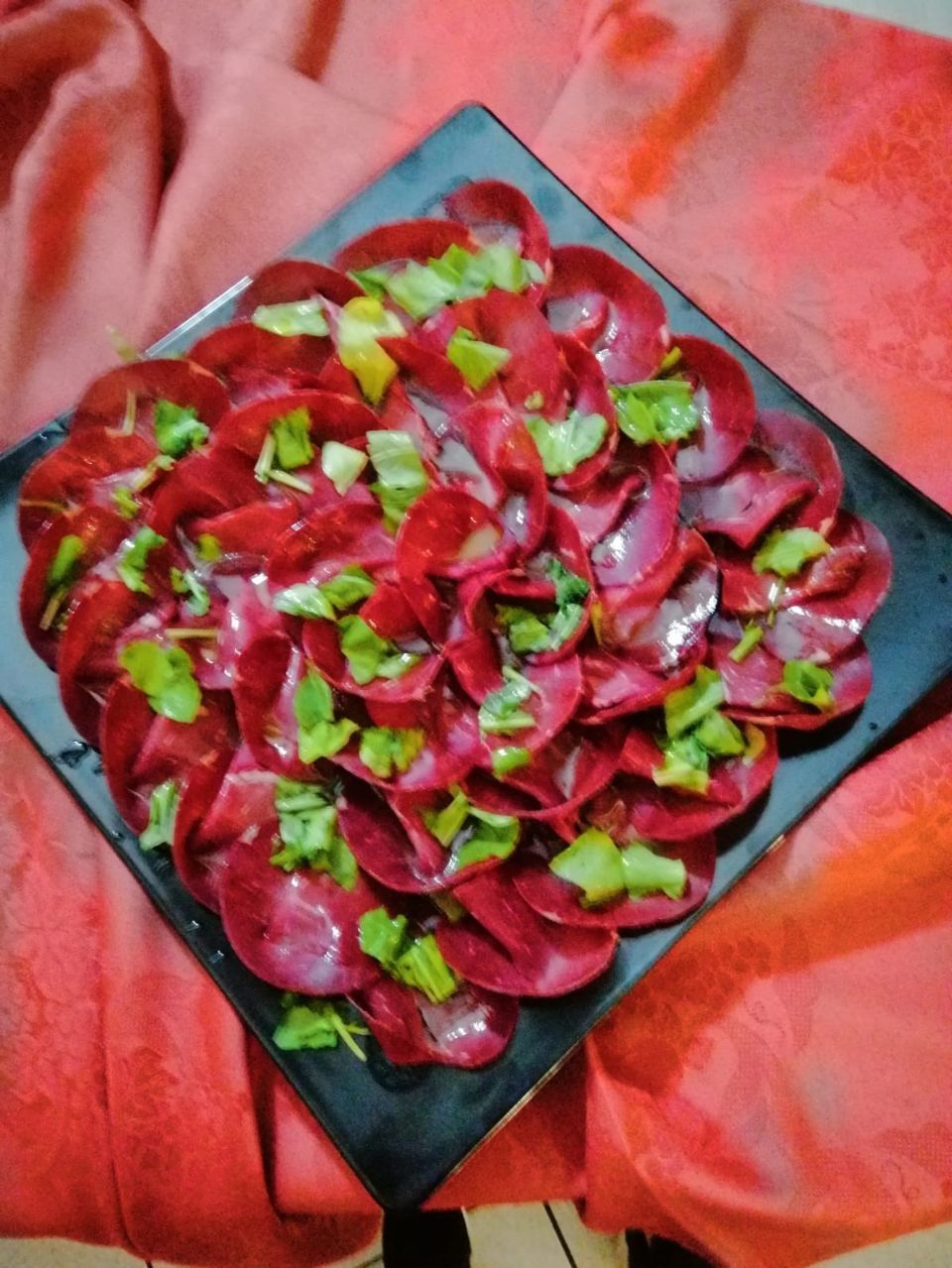 Insalata di barbabietole con erbe verdi su un piatto nero su uno sfondo rosso.