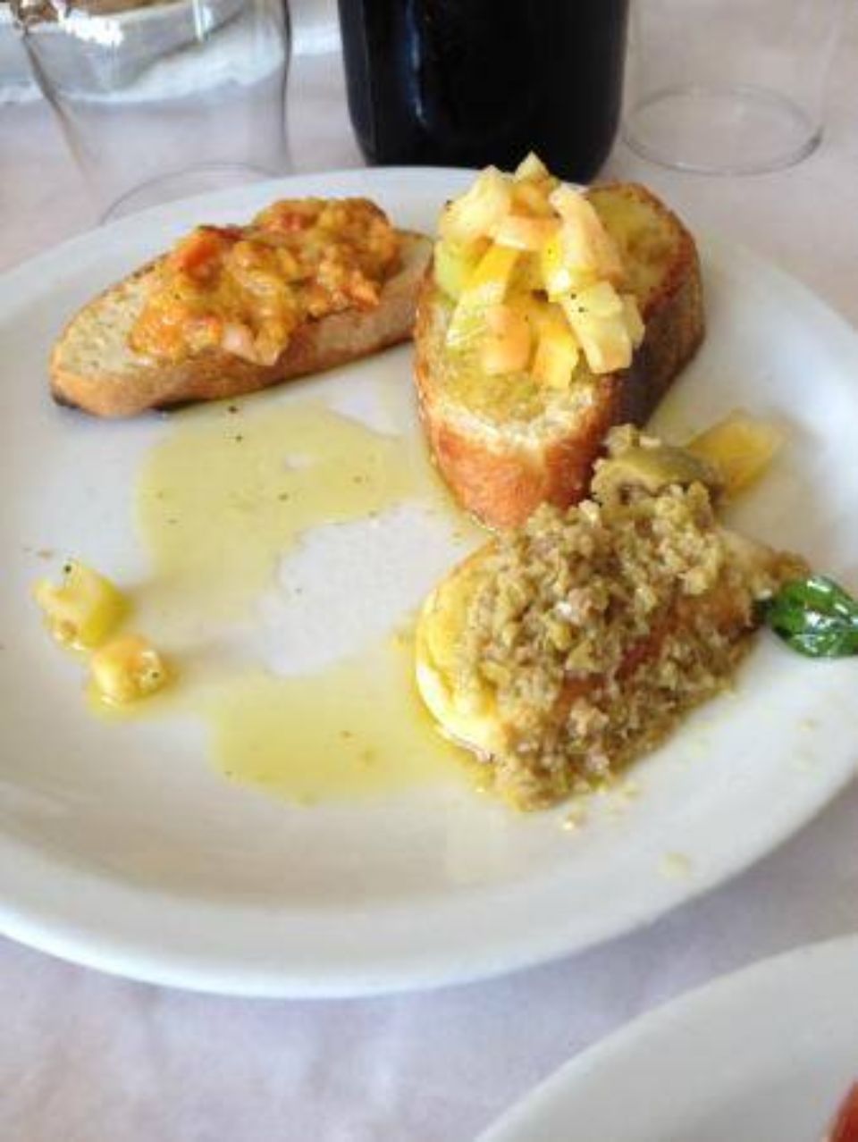 Piatto con tre bruschette: frutti di mare, verdure e tapenade di olive con olio.