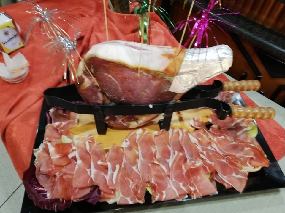 Esposizione di prosciutto crudo, con fette disposte su un vassoio. Il prosciutto è adagiato in un contenitore nero su un panno rosso.