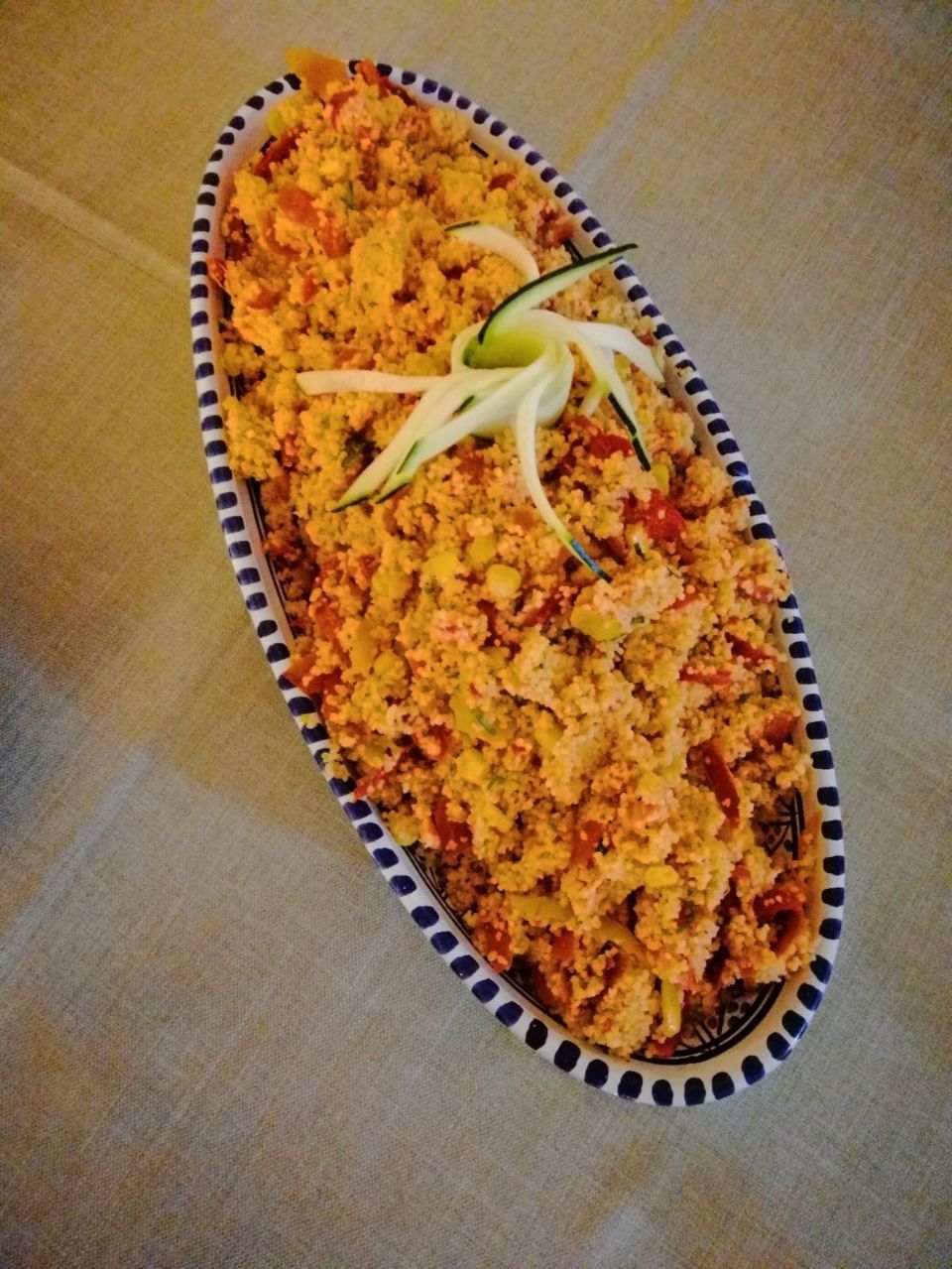 Un'insalata di couscous colorata servita in un piatto ovale blu e bianco, guarnito con cetriolo.