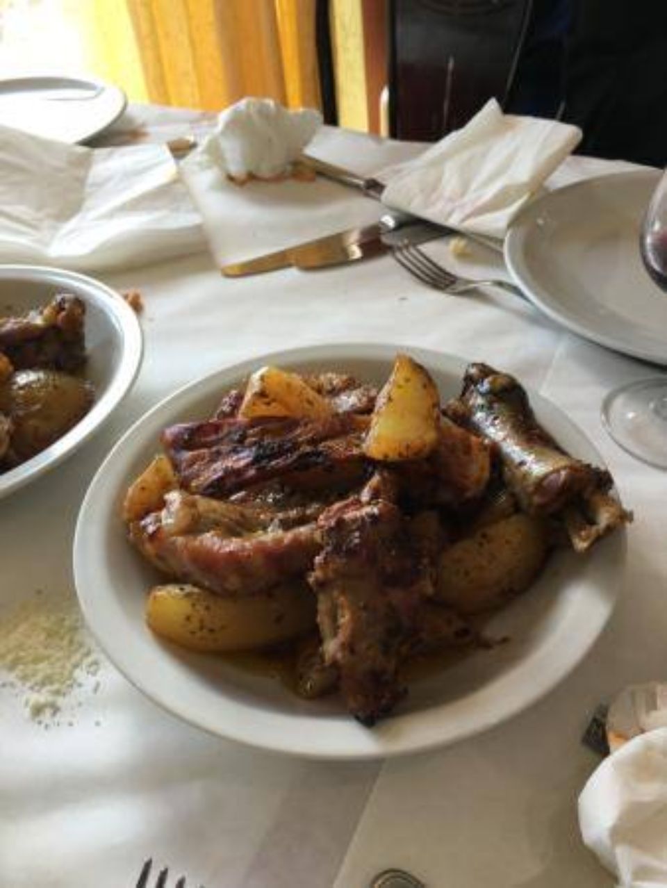 Piatto di patate arrosto, salsiccia e carne su una tovaglia bianca in un ristorante.