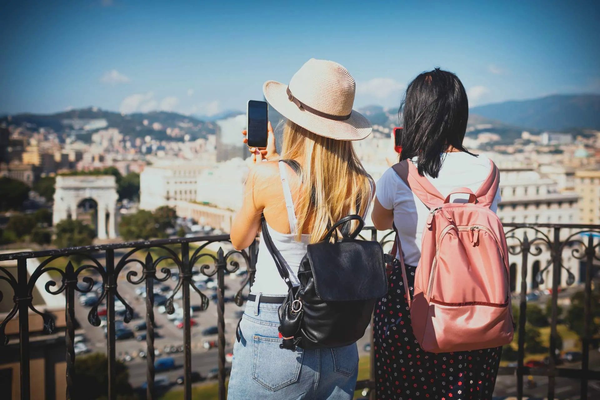 Due donne con zaini scattano foto di una vista della città con un telefono.