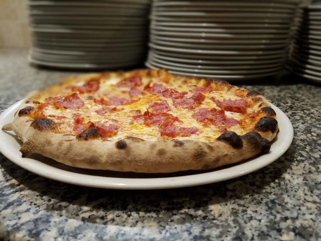 Pizza al pepperoni su un piatto bianco, con pile di piatti sullo sfondo su un bancone.