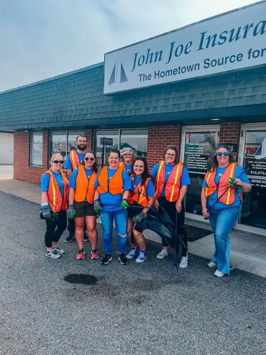 Group of volunteers in orange safety vests posing outside John Joe Insurance storefront.