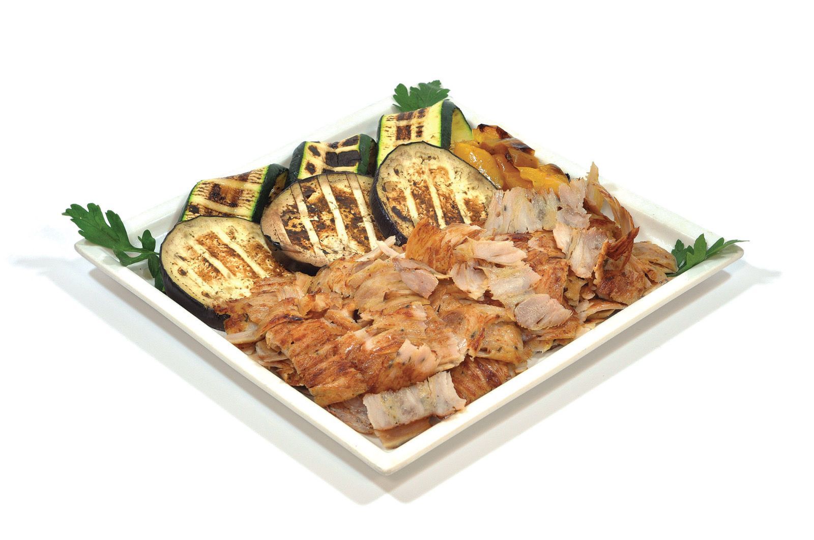 Un piatto quadrato contenente fette di carne grigliate e pezzi di verdure bruciacchiate, tra cui zucchine e melanzane.