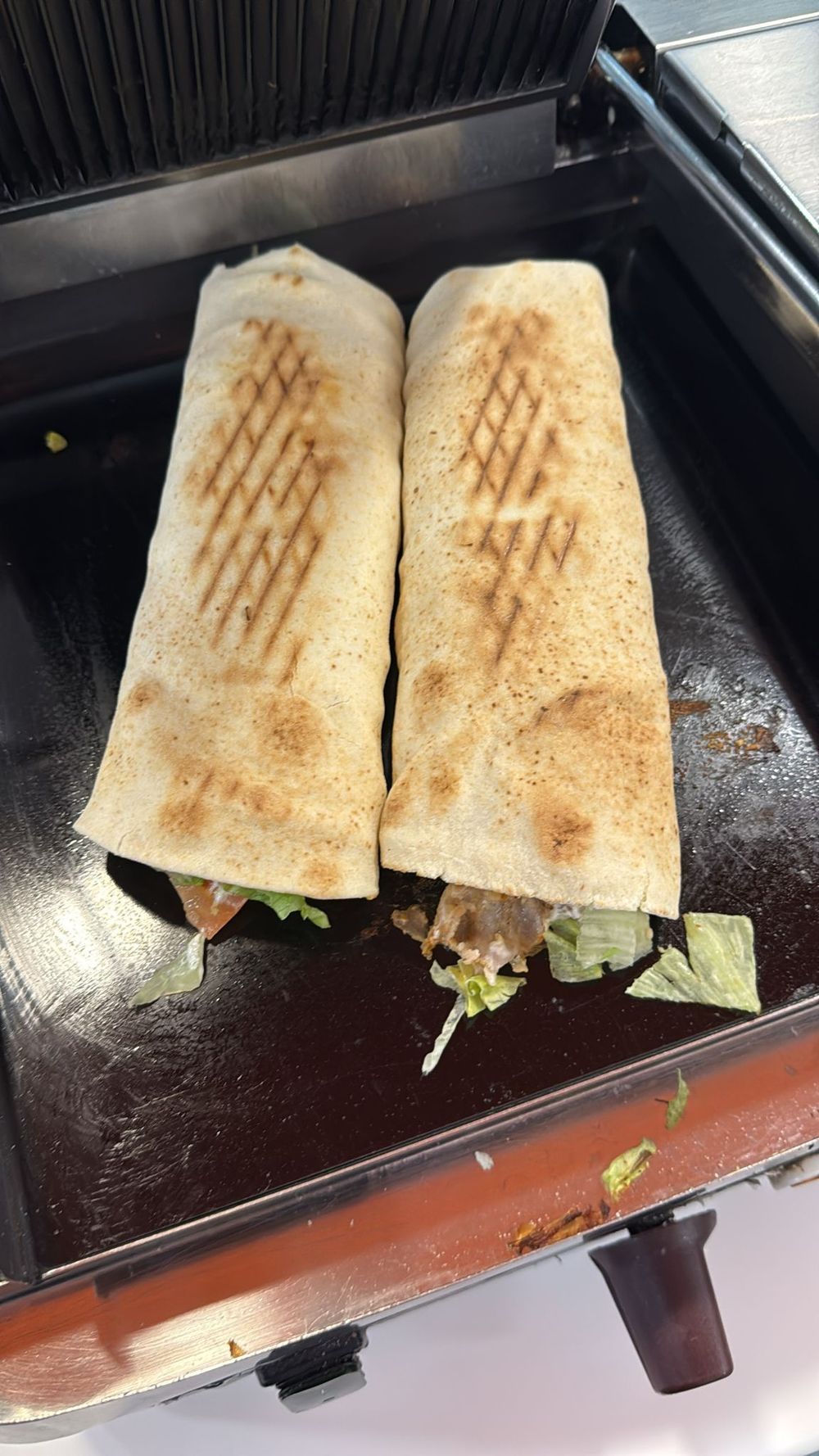 Due panini avvolti, con i segni della griglia, tostati su una piastra per panini nera.