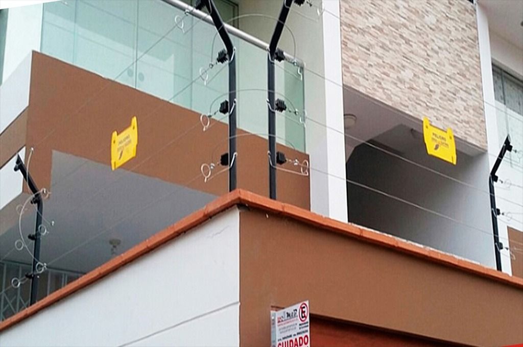 Cerca eléctrica en el perímetro de un edificio para mayor seguridad. Paredes marrones y blancas con señales de advertencia amarillas.
