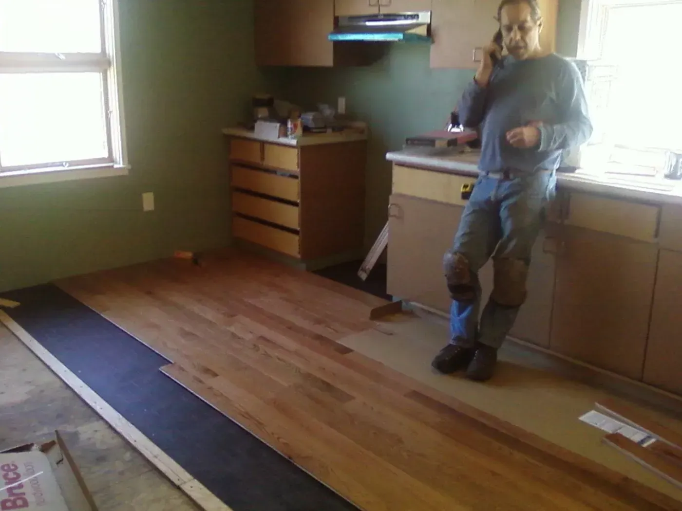 A man is standing in a kitchen talking on a cell phone