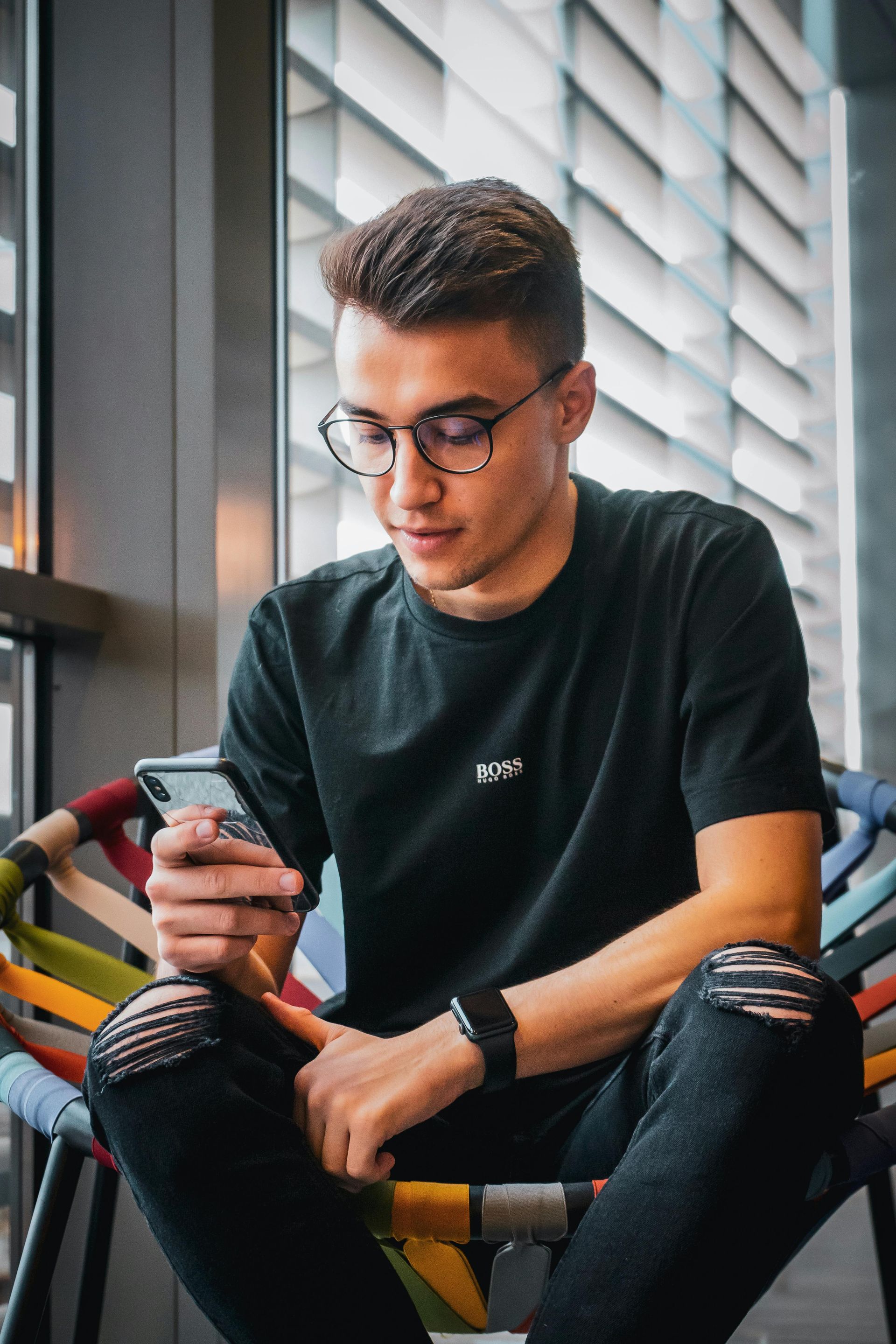 Young man with glasses looks at his phone while seated in a modern chair reviewing ibuyslabs graded card quote.