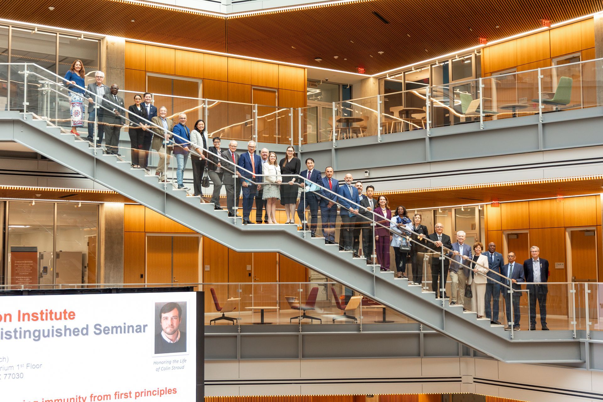 A large group stands on a modern, multi-level staircase inside a building during a Distinguished Seminar event.