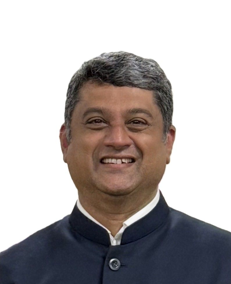 A smiling person with grey hair, wearing a dark blue mandarin-collar jacket over a white shirt, against a white background.