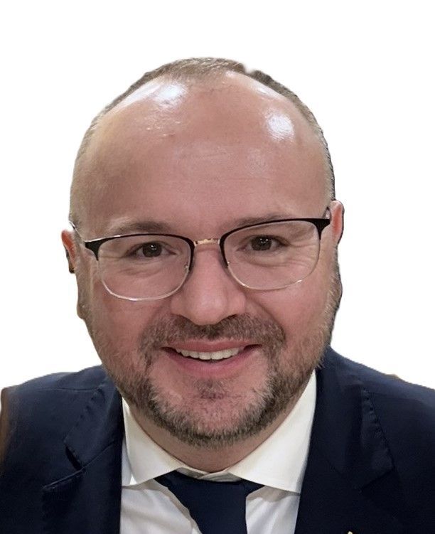A professional headshot of a person with short hair and glasses, wearing a dark suit, white shirt, and navy blue tie.