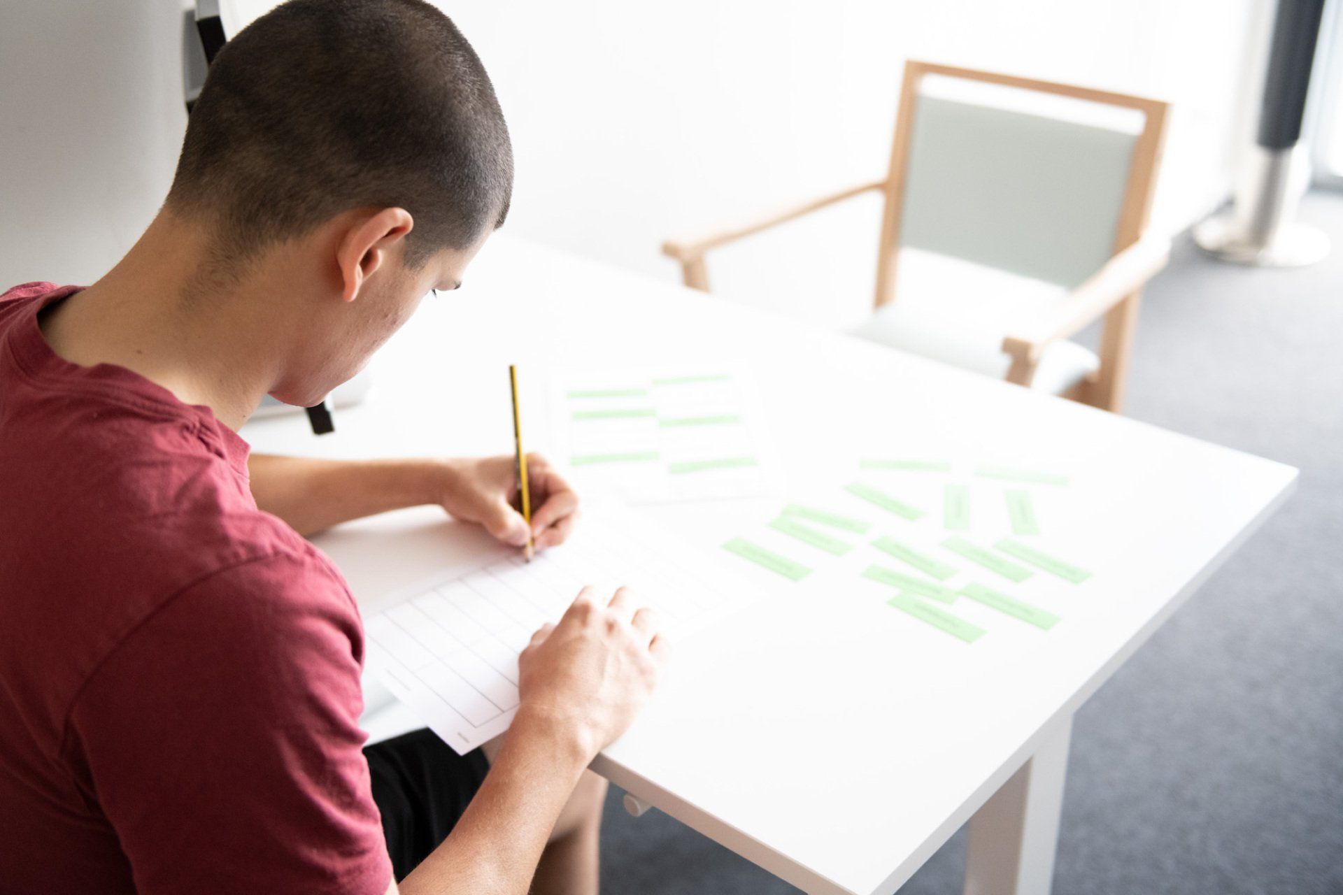 Ein Mann sitzt an einem Tisch und schreibt mit einem Bleistift auf ein Blatt Papier.