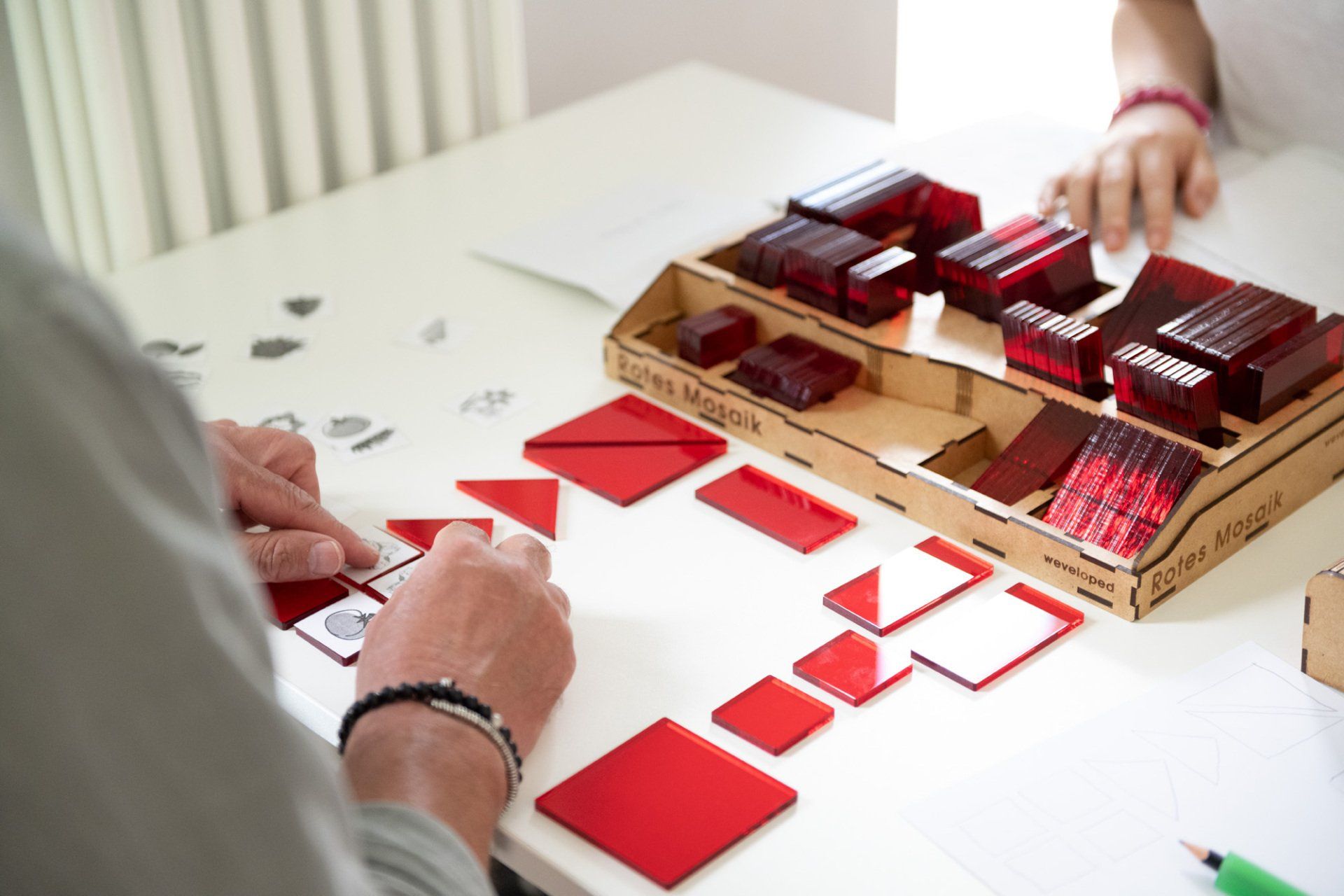 Eine Person spielt mit einer Schachtel roter Bauklötze auf einem Tisch