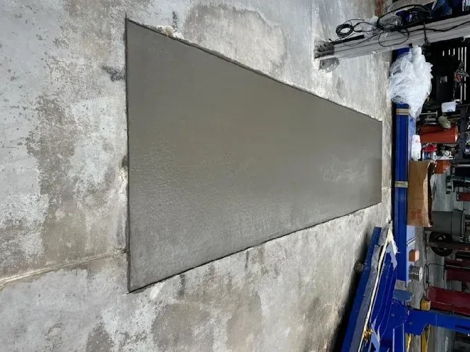 Freshly poured concrete rectangle in a garage, next to a car lift. Gray.
