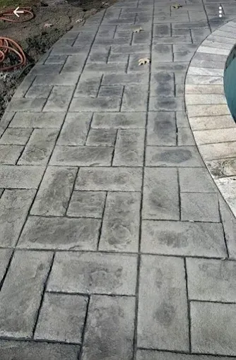 Gray stamped concrete pathway with a curved edge bordering a pool.