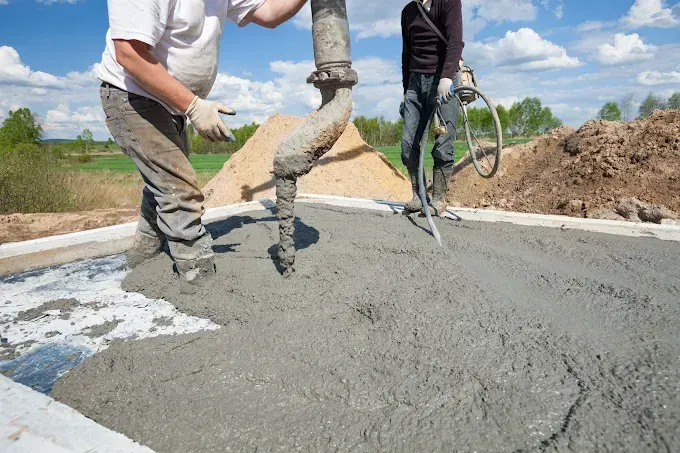 Workers pouring concrete foundation, using a pump in an outdoor setting.