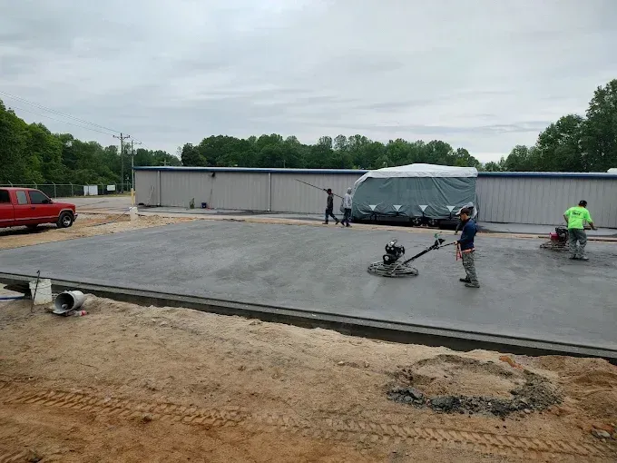 Workers smoothing wet concrete on a construction site; building in the background.