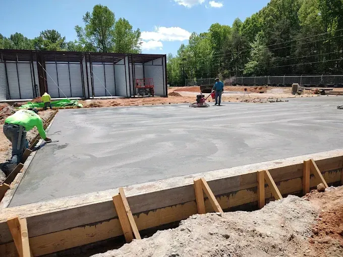 Workers smoothing a fresh concrete slab at a construction site. Wooden forms and metal framework visible.