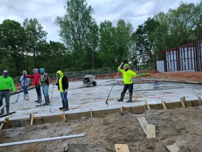 Construction workers smoothing concrete, on a gray day. One raises a tool. Wooden forms are in the foreground.
