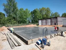 Construction site: workers finishing a concrete slab. A building frame is in the background. Sunny day.