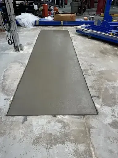 Freshly poured concrete rectangle on a shop floor.