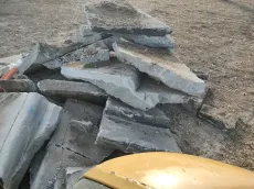 Pile of broken concrete slabs on dirt, likely construction debris.