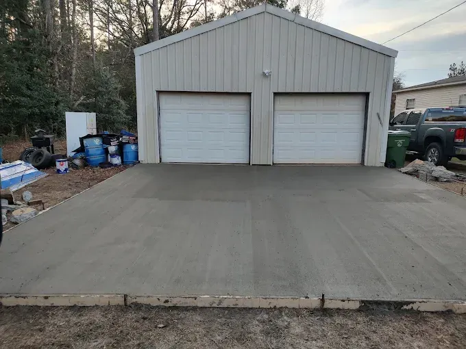 Freshly poured concrete driveway in front of a white metal two-car garage.