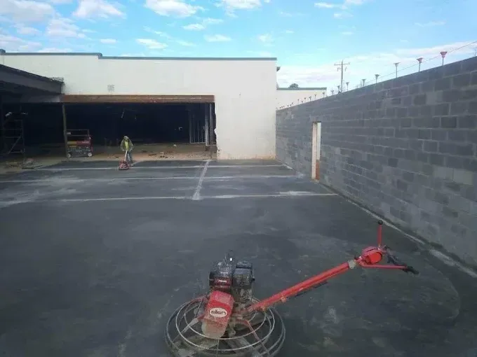 Concrete finishing machine on a newly poured concrete surface, with a building under construction in the background.