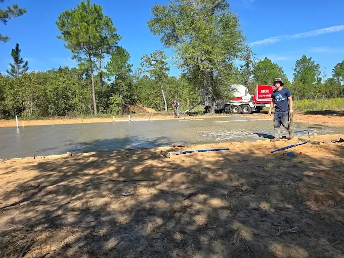 Construction workers pouring concrete slab; a cement truck is present; blue sky.