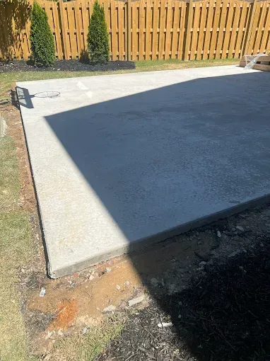 Newly poured concrete patio in a backyard setting, next to grass and fence.
