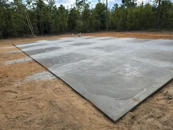 Concrete foundation in a dirt clearing, with trees in the background.