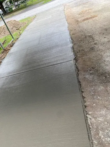 Newly poured concrete sidewalk next to gravel and a street.