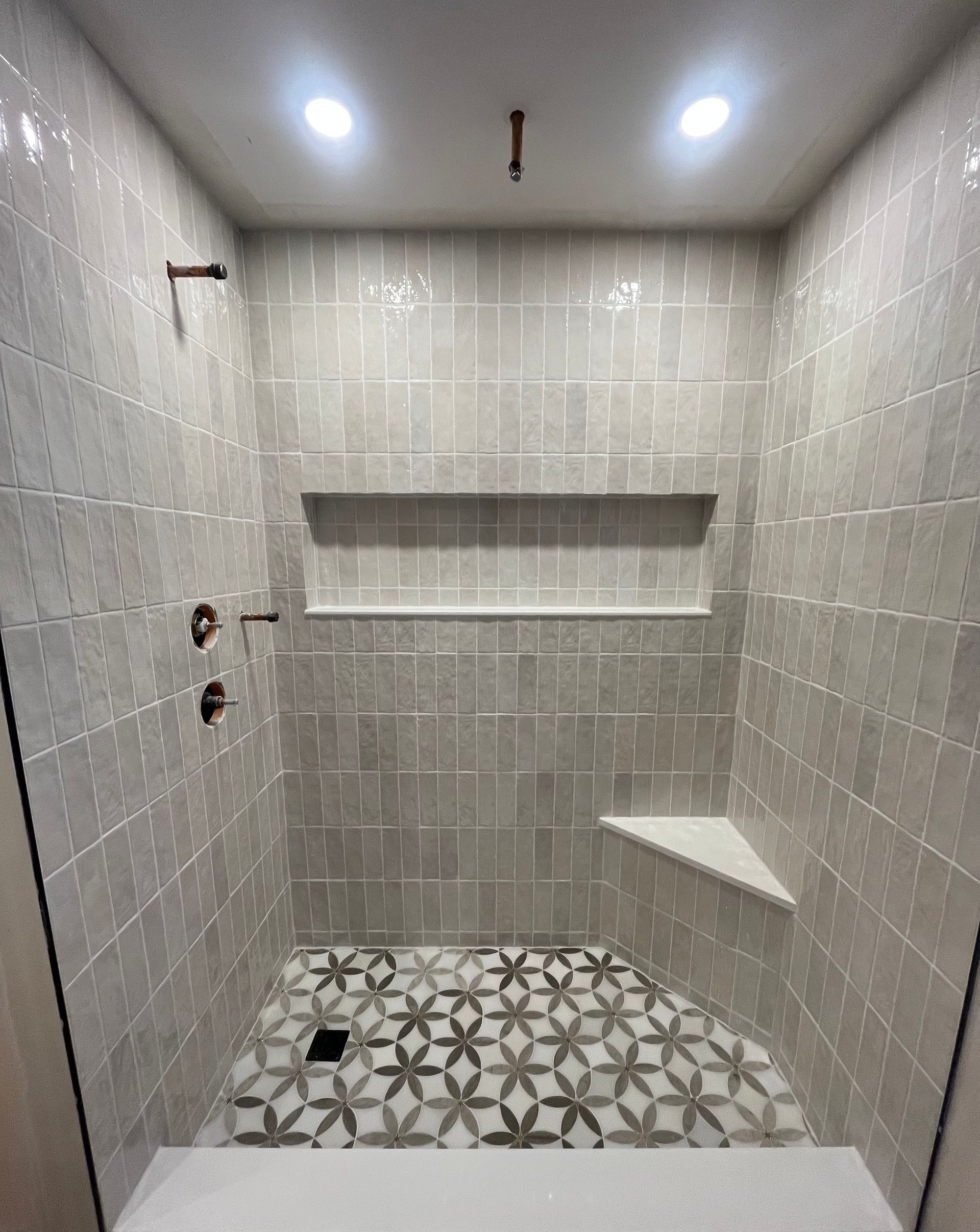 A tiled walk-in shower with light grey square wall tiles, a floral patterned floor, a built-in bench, and a wall niche.