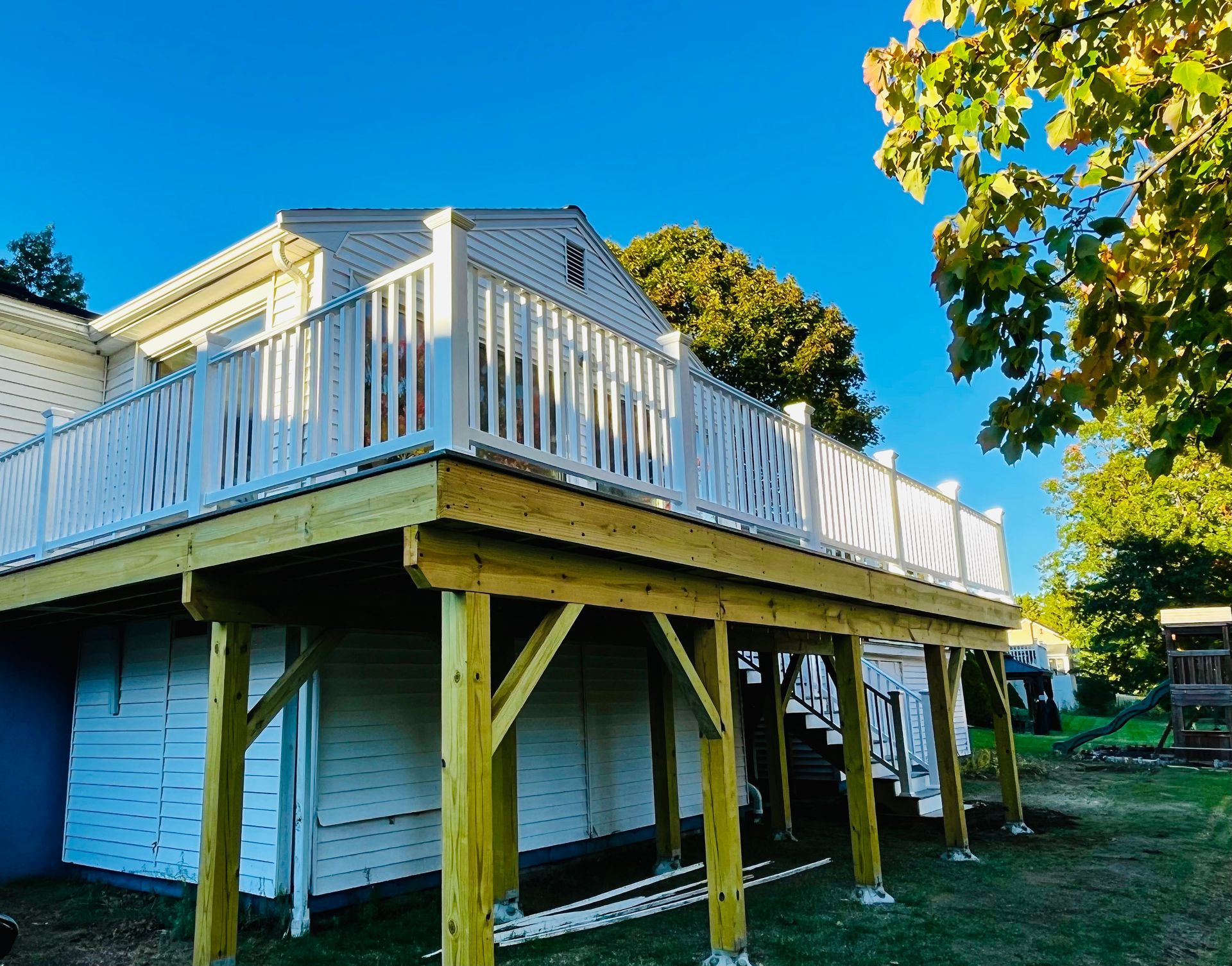 A wide, elevated wooden deck attached to the side of a white house with white railings, supported by yellow support beams.