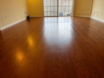 A room with warm-toned hardwood floors, light walls, and a large sliding glass door with a view of trees outside.