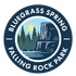 Circular logo of a sunset over a forest and rocky waterfall by a lake
