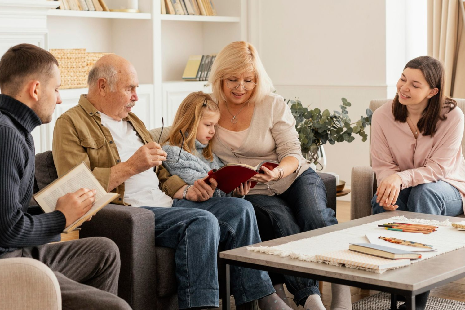 Family reading together in a living room: Grandparents, parents, and child reading a book.