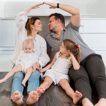 A family is sitting on the floor making a roof with their hands